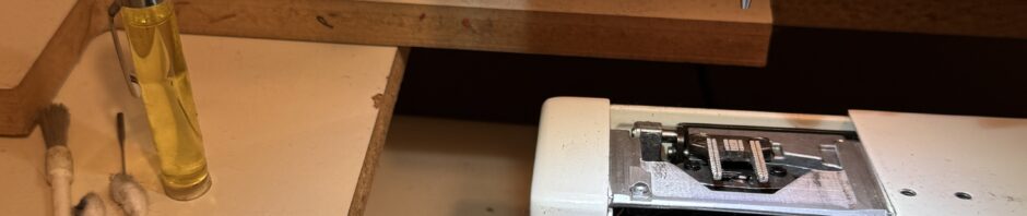 sewing machine cleaning in progress. Machine with bobbin area open. oil, tips, special screwdriver and brush sit to to left