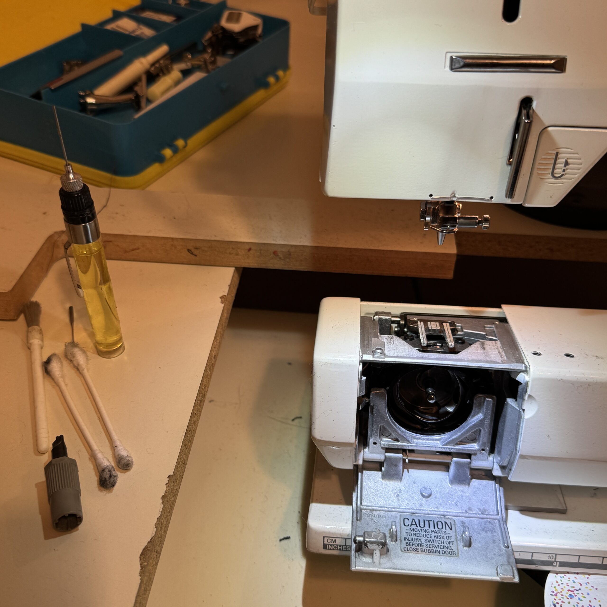 sewing machine cleaning in progress. Machine with bobbin area open. oil, tips, special screwdriver and brush sit to to left