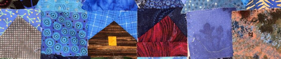 Pieces of fabric stuck to a wall, lots of blues, triangles, squares. a few pieced squares that look like simple houses - a roof and a window.